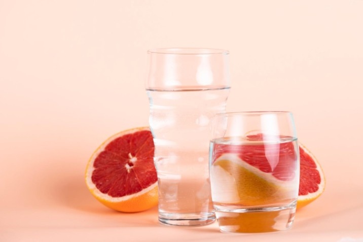 Two glasses of clear water and a sliced grapefruit against a soft peach-colored background.