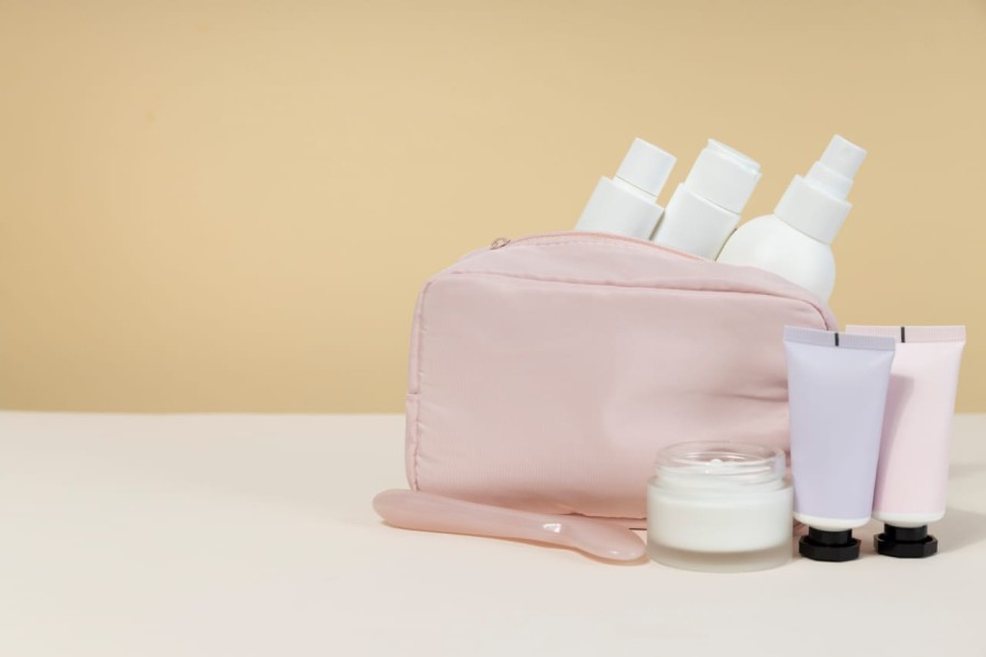 A collection of skincare products in white bottles and tubes arranged next to a light pink travel pouch.