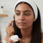 Woman applying face cream to acne-prone skin while looking in a mirror