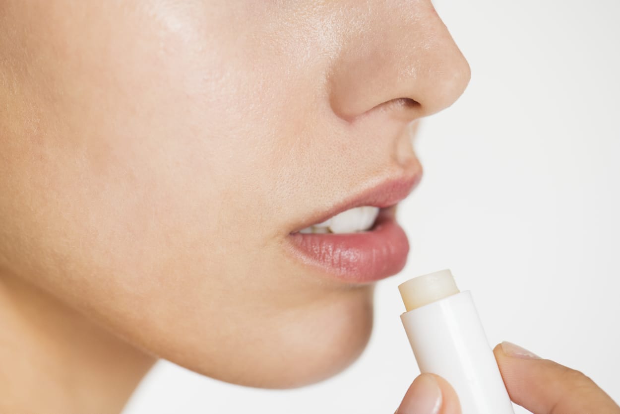 A close-up of a person applying a clear lip balm stick to their lips.