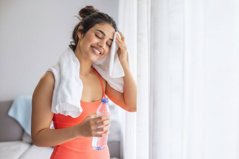 Woman wiping sweat with a towel while holding a water bottle after a workout